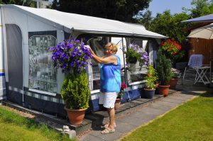 een vrouw bij een caravan met veel bloemen op de natuurcamping gelderland