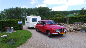 Een rode auto met een caravan op de kleine camping Limburg