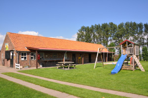 Een groot stenen gebouw en een speeltoestel op de boerencamping Overijssel