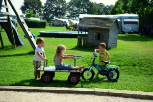 Drie kleine kinderen met een kar en een fiets op de kleine camping Drenthe