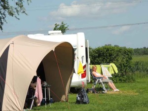 Een vouw zit voor de caravan in de zon op de boerencamping Utrecht