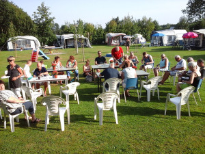 Mensen eten buiten aan tafels op het grasvel van een van de kleine campings Gelderland