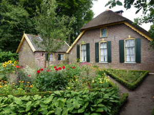 Een mooi oud gebouw mmet een rieten dak en een kleurrijke tuin