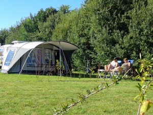 Een caravan met een voortent en twee mensen die in de zon zitten op een natuurcamping zuid holland