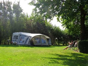 Mensen lezen op een stoeltje in de zon bij hun caravan op een natuurcamping zuid holland